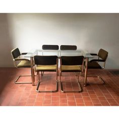 a glass table with chairs around it on a tile floor in front of a white wall