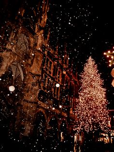 a large christmas tree is lit up in front of a church at night with snow falling on the ground