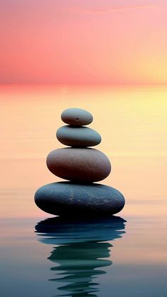 stack of rocks sitting on top of each other in the middle of water at sunset