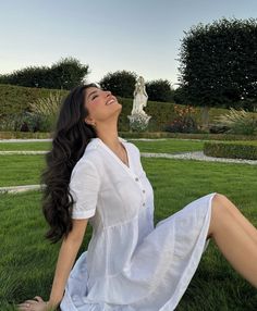 a woman sitting in the grass with her legs crossed and looking up to the sky