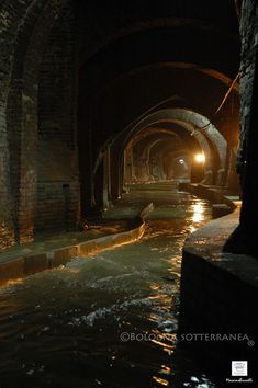 a dark tunnel with water running through it and lights on at the end in the distance