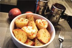 a white bowl filled with potatoes on top of a table next to two silver cups