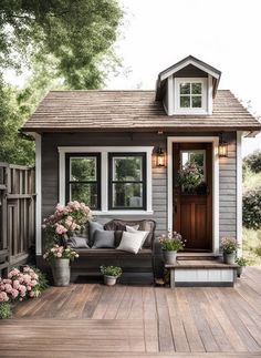 a small gray and white house with flowers on the porch