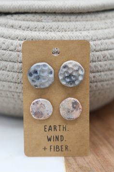 three pairs of earrings are sitting on a piece of cardboard next to a rope basket