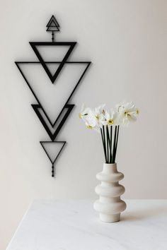 a vase with some flowers in it sitting on a table next to a wall sculpture