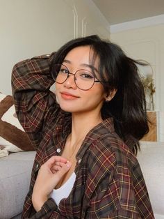 a woman wearing glasses sitting on a couch with her hands behind her head and looking at the camera