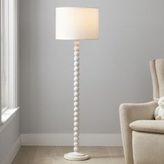 a white lamp sitting next to a chair in a living room with a teddy bear on the floor