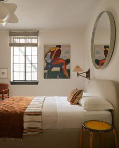 a bed sitting in a bedroom next to a window with two paintings on the wall