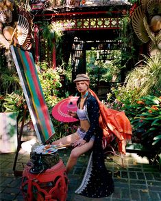 a woman sitting on top of a red bench in front of plants and umbrellas