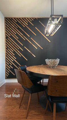 a dining room table with four chairs and a vase on the top of it in front of a black wall