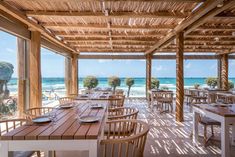 an outdoor dining area with wooden tables and chairs overlooking the ocean on a sunny day