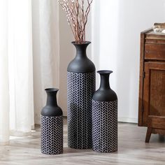 three black vases sitting on top of a wooden floor