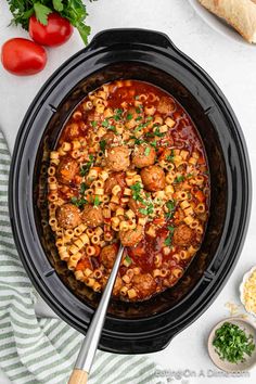 a crock pot filled with pasta and meatballs on top of a white table