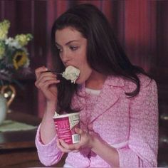 a woman in pink is eating something out of her mouth and holding a can of ice cream