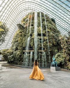 a woman is standing in front of a waterfall at the gardens by the bay, singapore