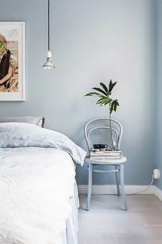 a bedroom with blue walls and white bedding has a plant on the nightstand next to it