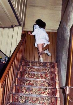 a woman in white shirt and shorts walking down stairs with rugs on the floor