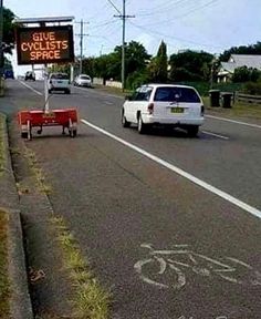 a white car driving down a street next to a sign that says give cyclists space