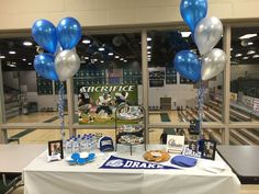 a table with balloons and pictures on it in front of a large window at a sports event