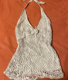 a white crocheted halter top laying on an orange sheet with a knot at the neck