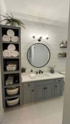 a bathroom with gray cabinets and white towels on the shelves, along with a large round mirror