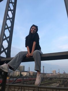 a woman sitting on top of a metal rail next to a train track with buildings in the background