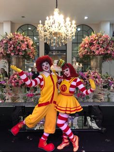 two clowns are posing for a photo in front of a table with flowers and chandeliers