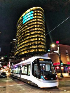 a white and black train traveling past tall buildings in the city at night with lights on