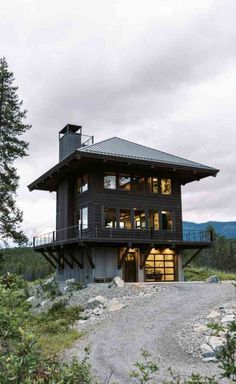 a large black house sitting on top of a lush green hillside next to a forest