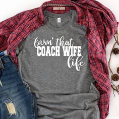 a gray shirt with the words cabin that coach wife life on it next to jeans and pine cones