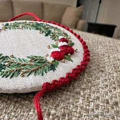 an embroidered christmas ornament with red flowers and greenery is on the table