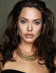 a close up of a woman with long hair and jewelry on her neck, looking at the camera