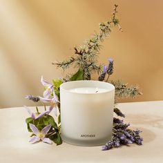 a white candle sitting on top of a table next to purple flowers and greenery