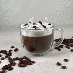 a glass mug filled with hot chocolate and marshmallows on top of coffee beans