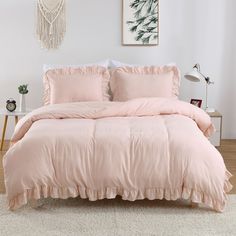 a bed with pink comforter and pillows in a white room next to a painting