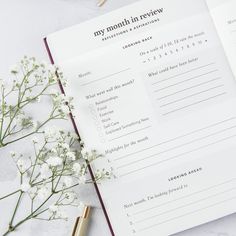 an open book with writing on it next to some white flowers and a gold pen