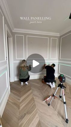 two people are taking pictures in the corner of a room with wood floors and white walls