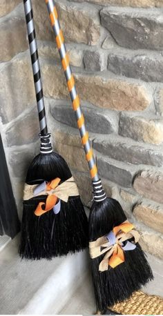 two black brooms with orange and white bows on them sitting next to a brick wall