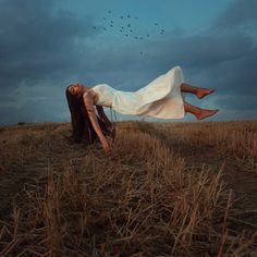 a woman laying in the middle of a field with birds flying overhead and her legs spread out