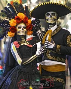 two people dressed in skeleton costumes with flowers on their head and one holding a fan