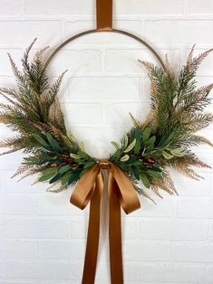 a wreath hanging on a brick wall with a brown ribbon around it and some greenery