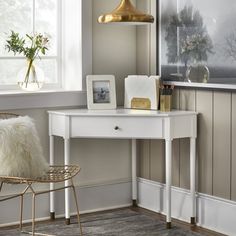 a white desk with a gold lamp and some pictures on the wall next to it