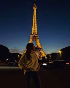 a woman standing in front of the eiffel tower at night