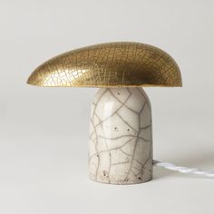 a white and gold table lamp sitting on top of a white surface with a cord attached to it