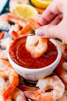 someone dipping shrimp into a bowl of marinara sauce