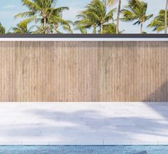 an empty swimming pool with palm trees in the background and a wooden wall behind it