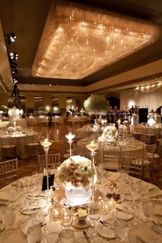 a banquet hall filled with lots of tables covered in white linens and centerpieces