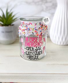 a glass jar filled with sprinkles on top of a white table next to a potted plant