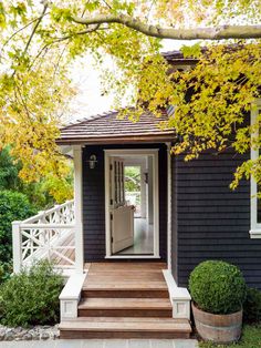 a black house with white trim and wooden steps leading to the front door is surrounded by greenery