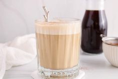 a glass filled with liquid sitting on top of a white counter next to a bowl